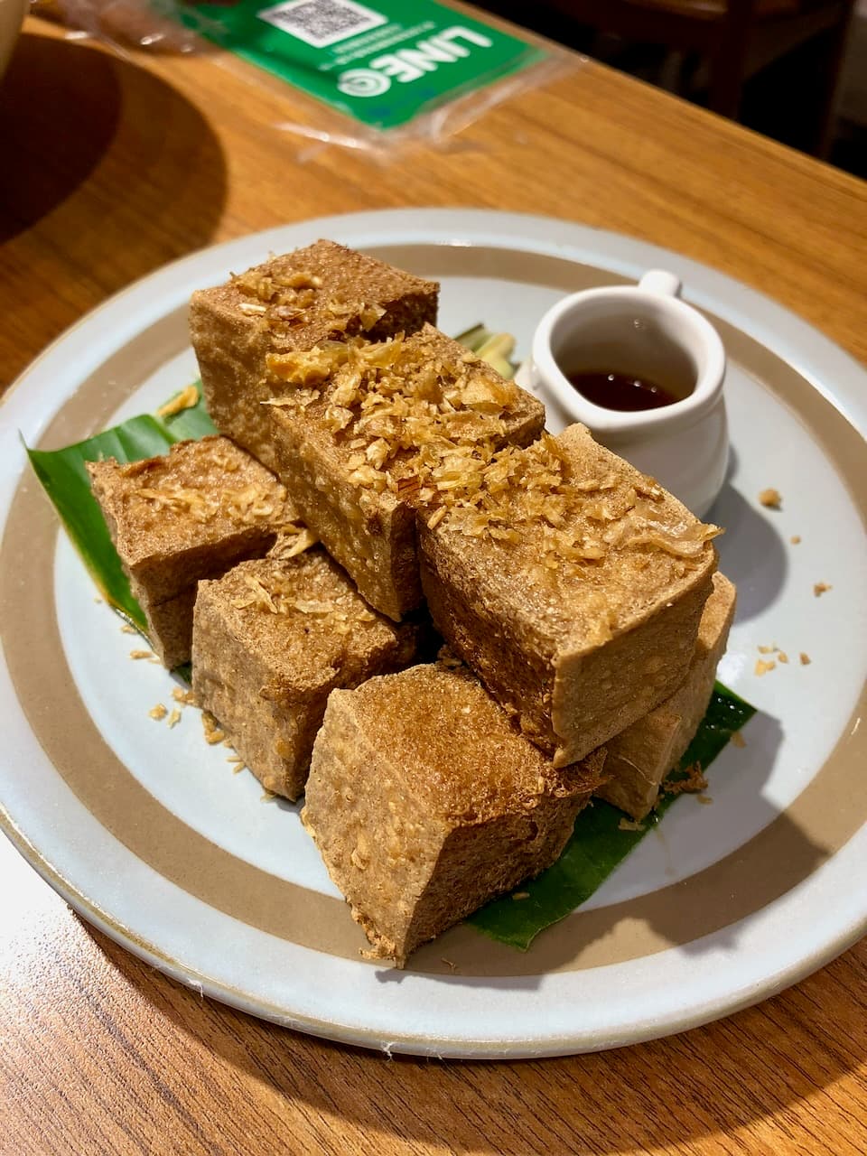 阮小越的炸豆腐，切成大塊墊著香蕉葉，旁邊一小壺醬汁